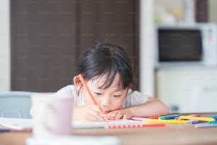 Asian girl drawing with colorful pens at the dining table at home