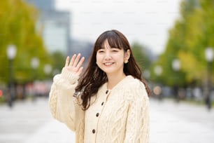 手のひらを振って笑顔で挨拶するアジア人(日本人)の若い女性