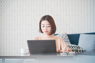 Joven asiática trabajando de forma remota con una computadora portátil en la habitación de su casa