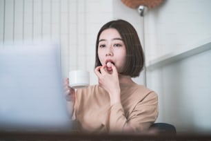 Asiatische junge Frau, die zu Hause auf den Laptop-Bildschirm im Zimmer schaut