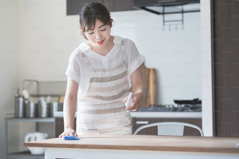 Mujer asiática limpiando la mesa de comedor de la casa con spray desinfectante y trapo