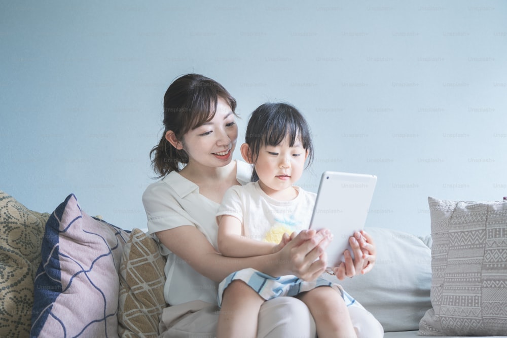 Mom and daughter sitting on a sofa and operating a tablet device