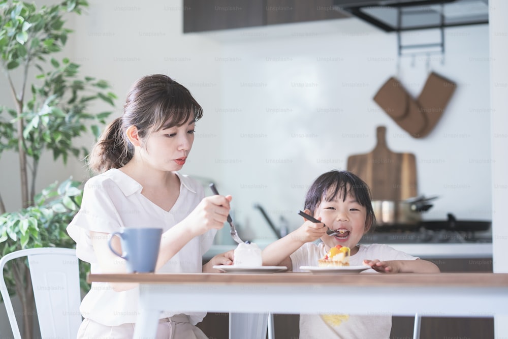 Mãe e filha asiáticas comendo bolo na mesa de jantar em casa