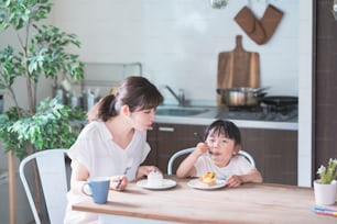 Asian mom and daughter eating cake at dining table at home