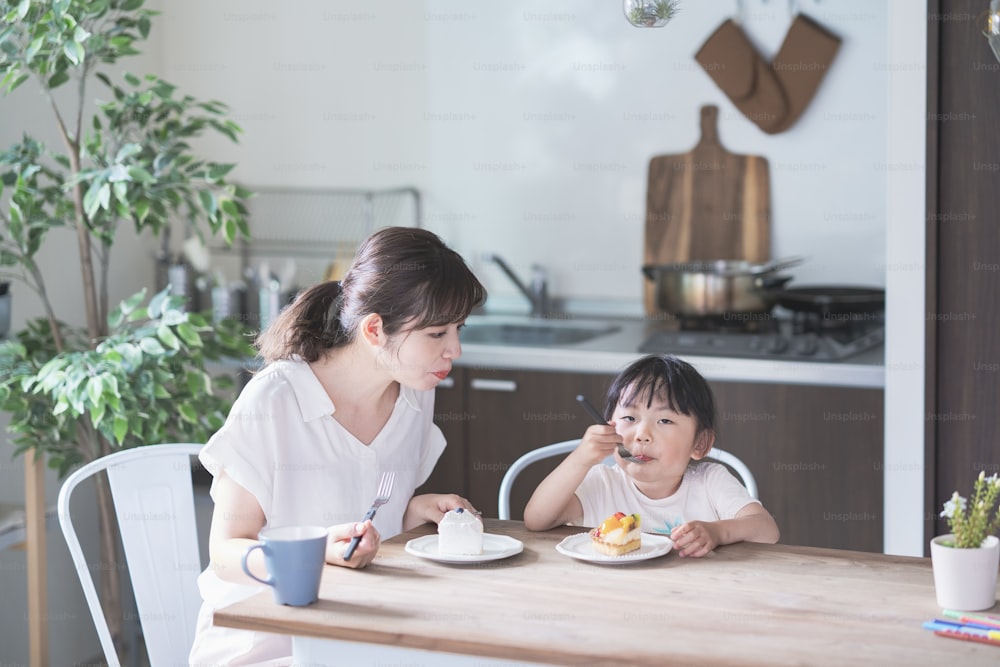 Asian mom and daughter eating cake at dining table at home