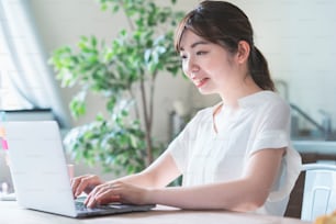 Asiatische Frau, die Remote-Arbeit mit Laptop am Esstisch zu Hause macht
