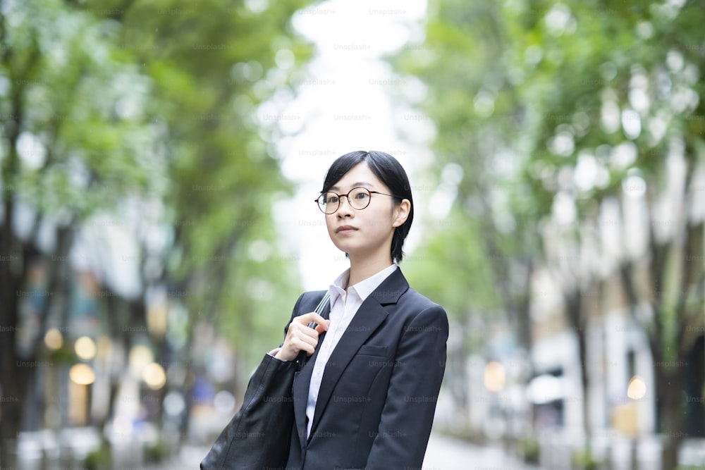 A young woman in a suit standing on a street lined with roadside trees