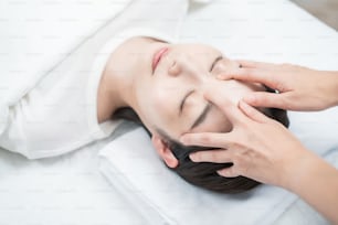 Giovane donna asiatica la cui testa viene massaggiata in un salone di estetica