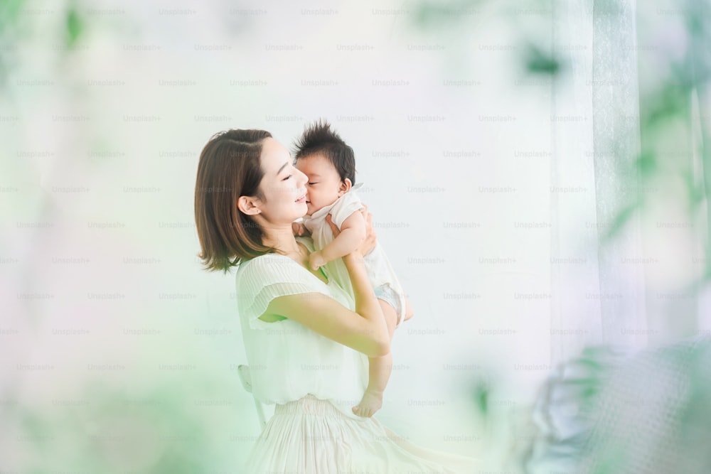 Asiatische Mutter hält ein Baby im hellen Raum