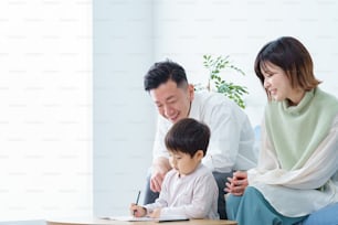 Un niño trabajando dibujando con un lápiz y sus padres cuidándolo