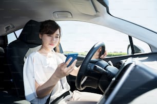 ハンドルを握るスマートフォンを使用する若い女性ドライバー。