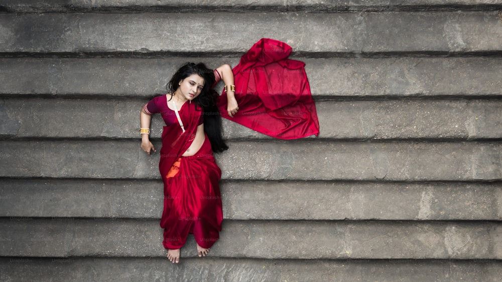 伝統的なインドの赤いサリー、金の宝石、腕輪を身に着けた遺産の階段井戸にある美しいインドの女の子のポートレート。マードゥルガーアゴモニ撮影コンセプト。ポーズを持つ階段の伝統的な女性