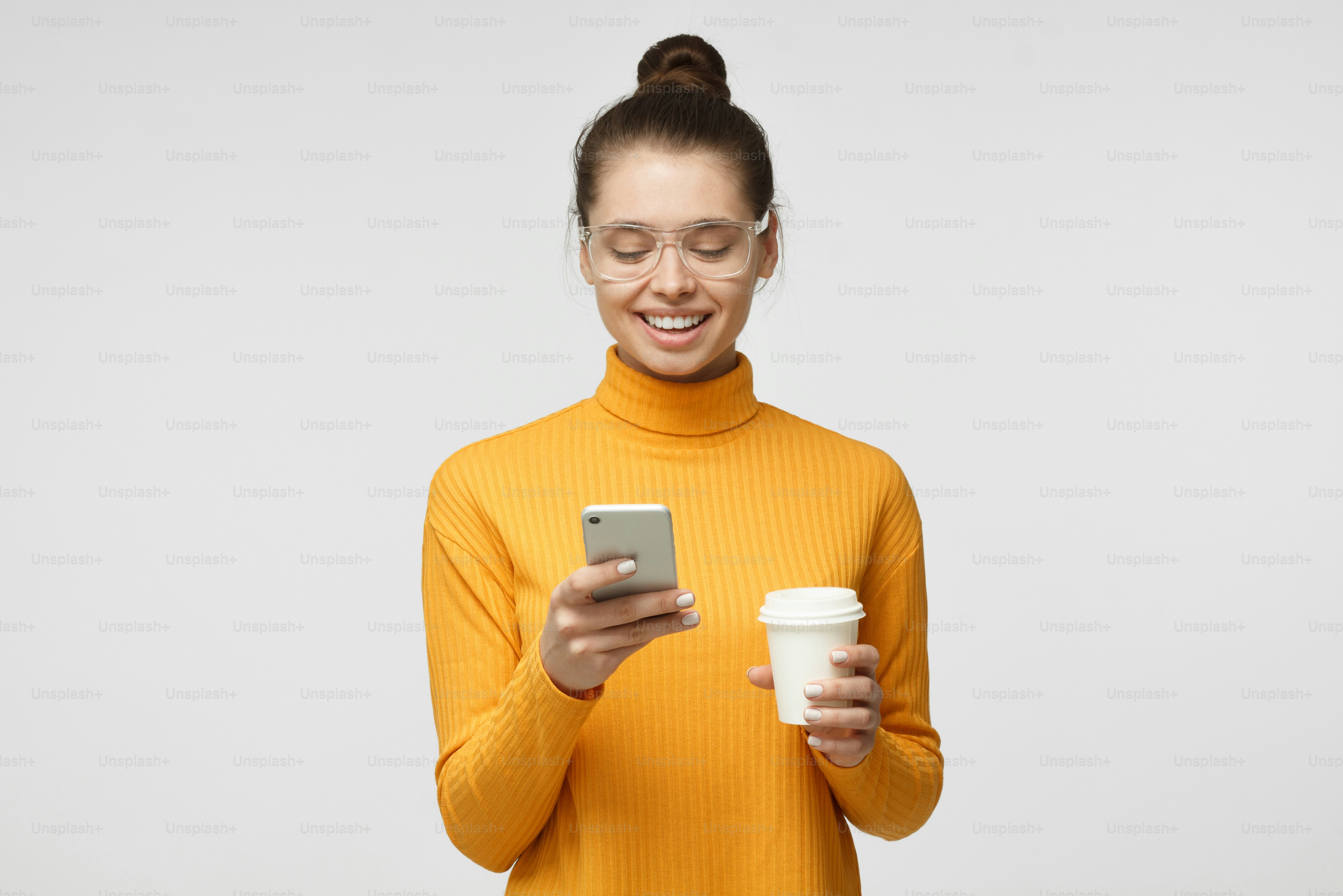 Indoor picture of young good-looking European woman isolated on gray background holding phone in hand, looking to screen smiling while browsing or reading message