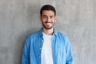 Closeup picture of young European male isolated on grey background wearing casual clothes and posing in studio, feeling calm and relaxed as if enjoying his free time alone or willing to go somewhere