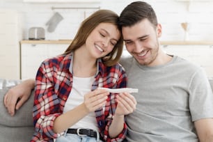 Happy couple looking at positive results of pregnancy test, planning future family life with child