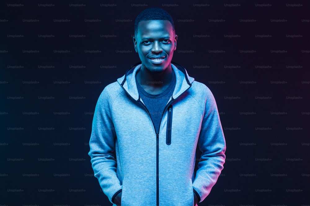 Ritratto al neon scuro dell'uomo africano sorridente che indossa felpa grigia