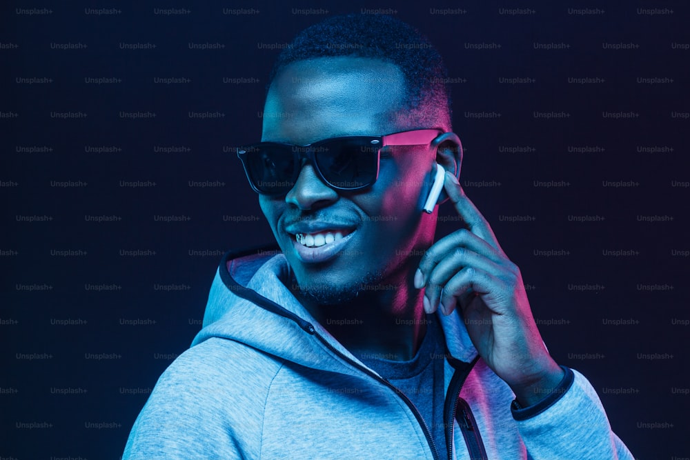 Neonporträt eines jungen afrikanischen Mannes, der Musik mit drahtlosen Kopfhörern hört