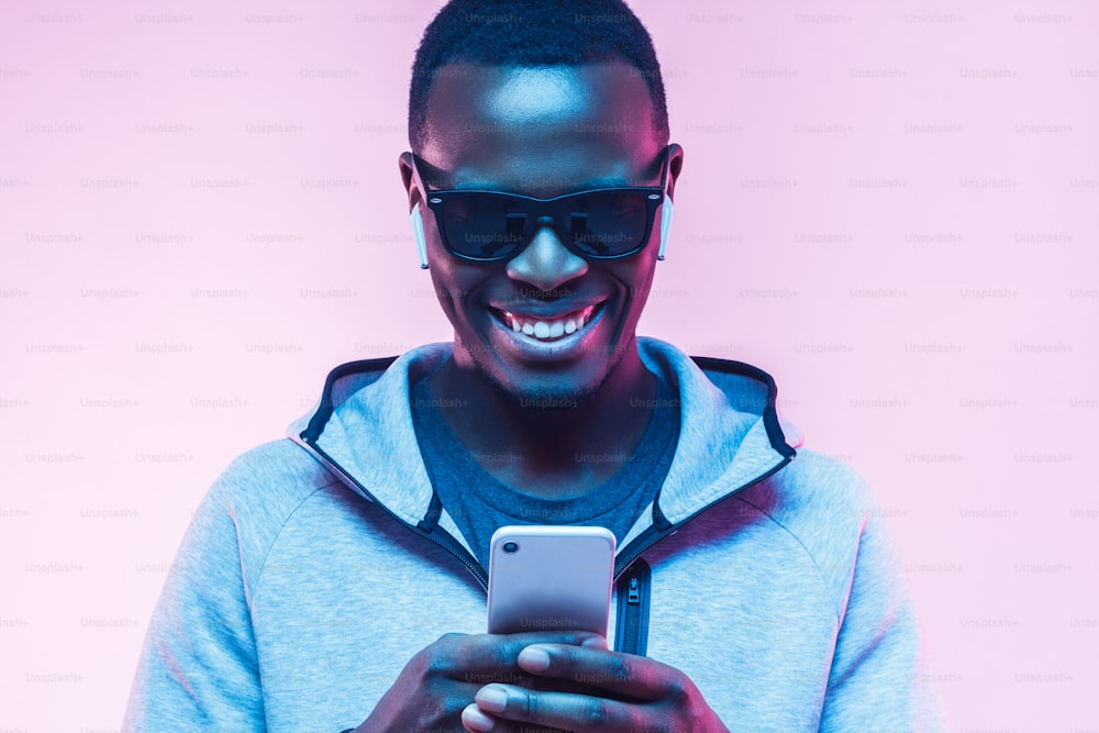 Neon-Porträt eines glücklichen jungen afrikanischen Mannes, der auf das Handy schaut