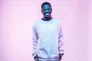 Young african american man standing with hands in pockets, wearing blank white swearshirt with copy space for your logo or text, isolated on pink background