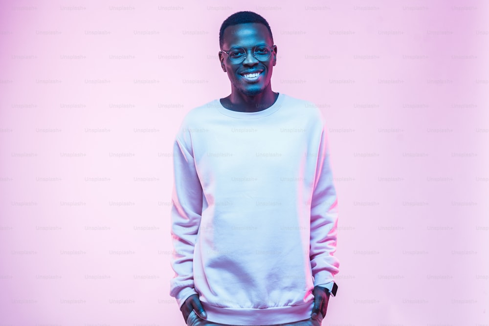 Jeune homme afro-américain debout, les mains dans les poches, portant une chemise blanche vierge avec un espace de copie pour votre logo ou votre texte, isolé sur fond rose
