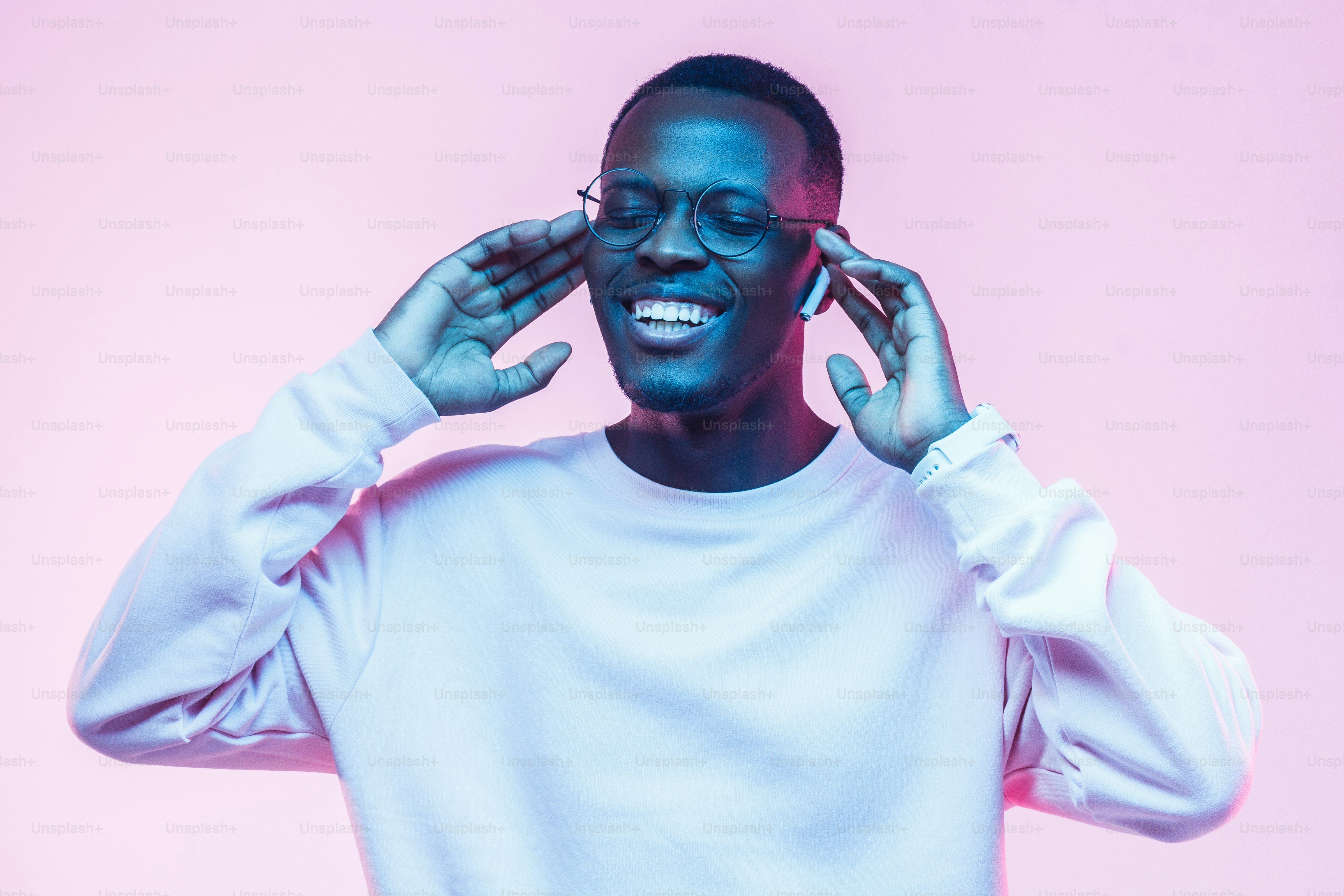 Joven y guapo hombre afroamericano, auriculares inalámbricos y escuchando su canción favorita, bailando, sonriendo con los ojos cerrados