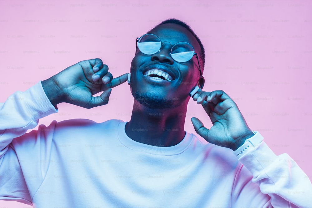 Joven africano escuchando música con auriculares, bailando aislado sobre fondo rosa