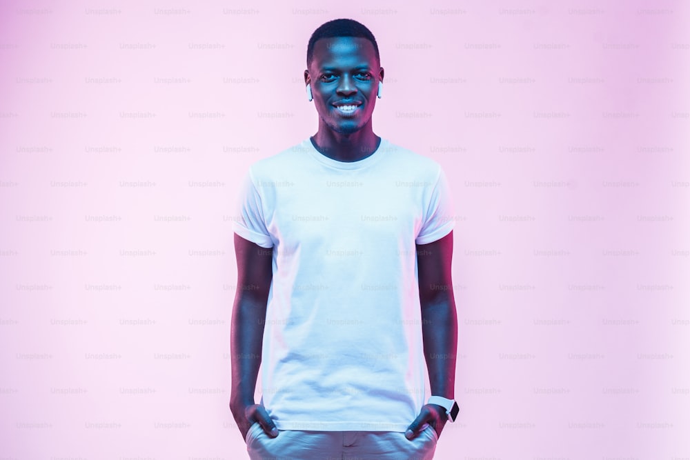 Attraktiver junger afrikanischer Mann, der in einem leeren weißen Baumwoll-T-Shirt posiert und isoliert auf rosa Hintergrund steht