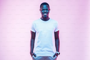 Attractive young african man posing in blank white cotton t-shirt, standing isolated on pink background
