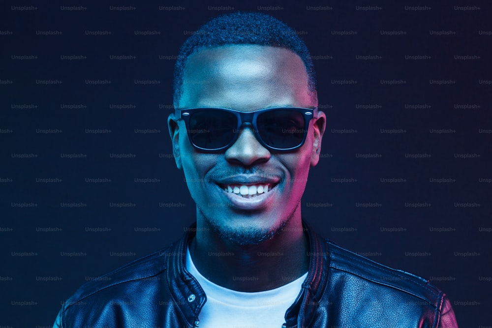 Close-up studio shot of smiling african american male model wearing trendy sunglasses and leather jacket