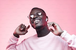 Jovem africano ouvindo música com fones de ouvido, dançando isolado no fundo rosa