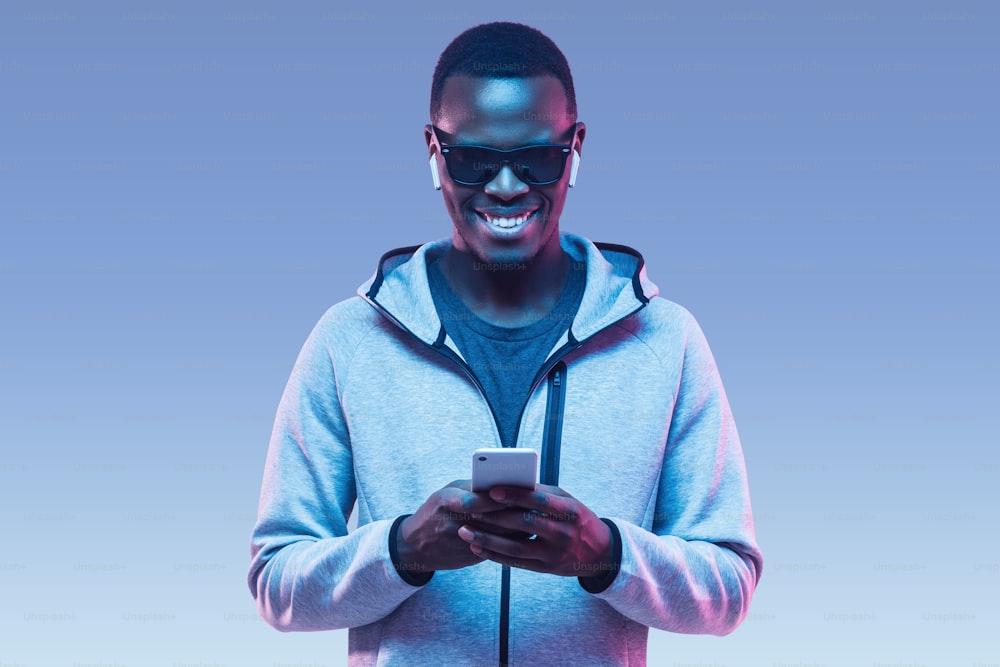 Ritratto di giovane uomo afroamericano che usa lo smartphone per ascoltare musica con gli auricolari