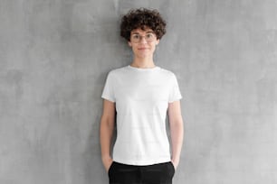 Jolie jeune femme posant dans un t-shirt en coton blanc vierge, debout contre un mur texturé gris