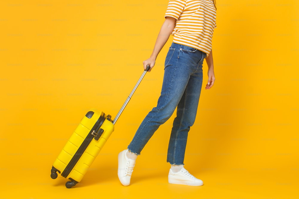Concepto de viajes y turismo. Mujer joven vestida con ropa casual caminando con maleta aislada sobre fondo amarillo