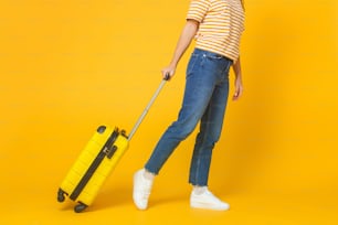Travel and tourism concept. Young woman wearing casual clothes walking with suitcase isolated on yellow background