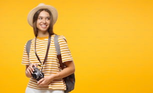 黄色い背景にカメラを持つ笑顔の若い女性観光客の水平バナー、コピー用スペース