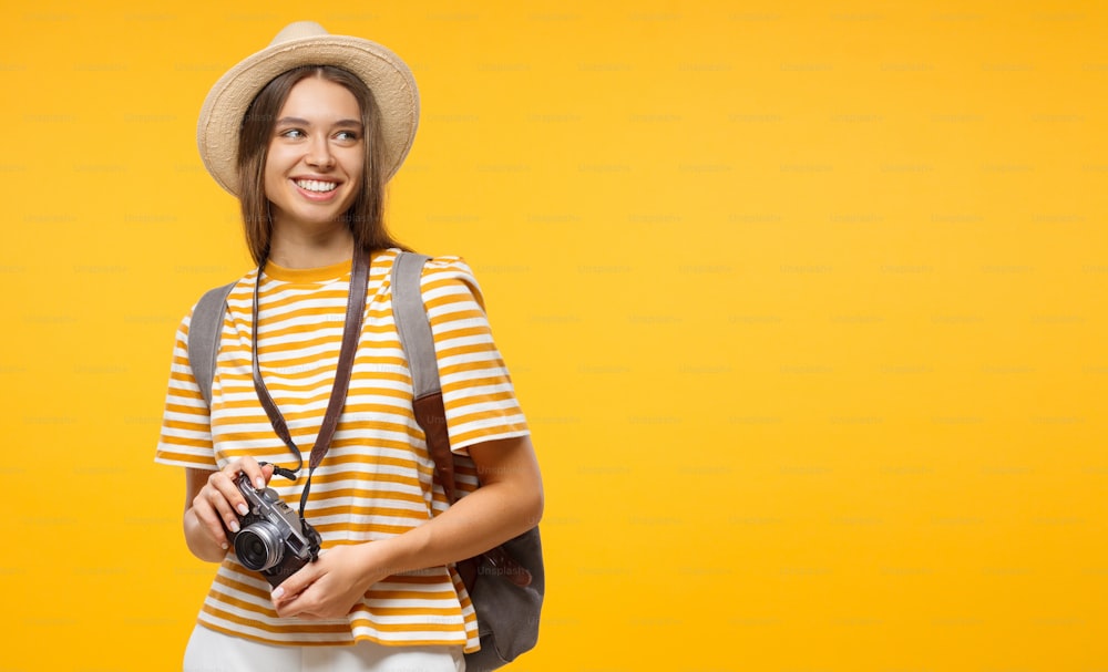 Horizontal banner of smiling young female tourist holding camera, isolated on yellow background with copy space