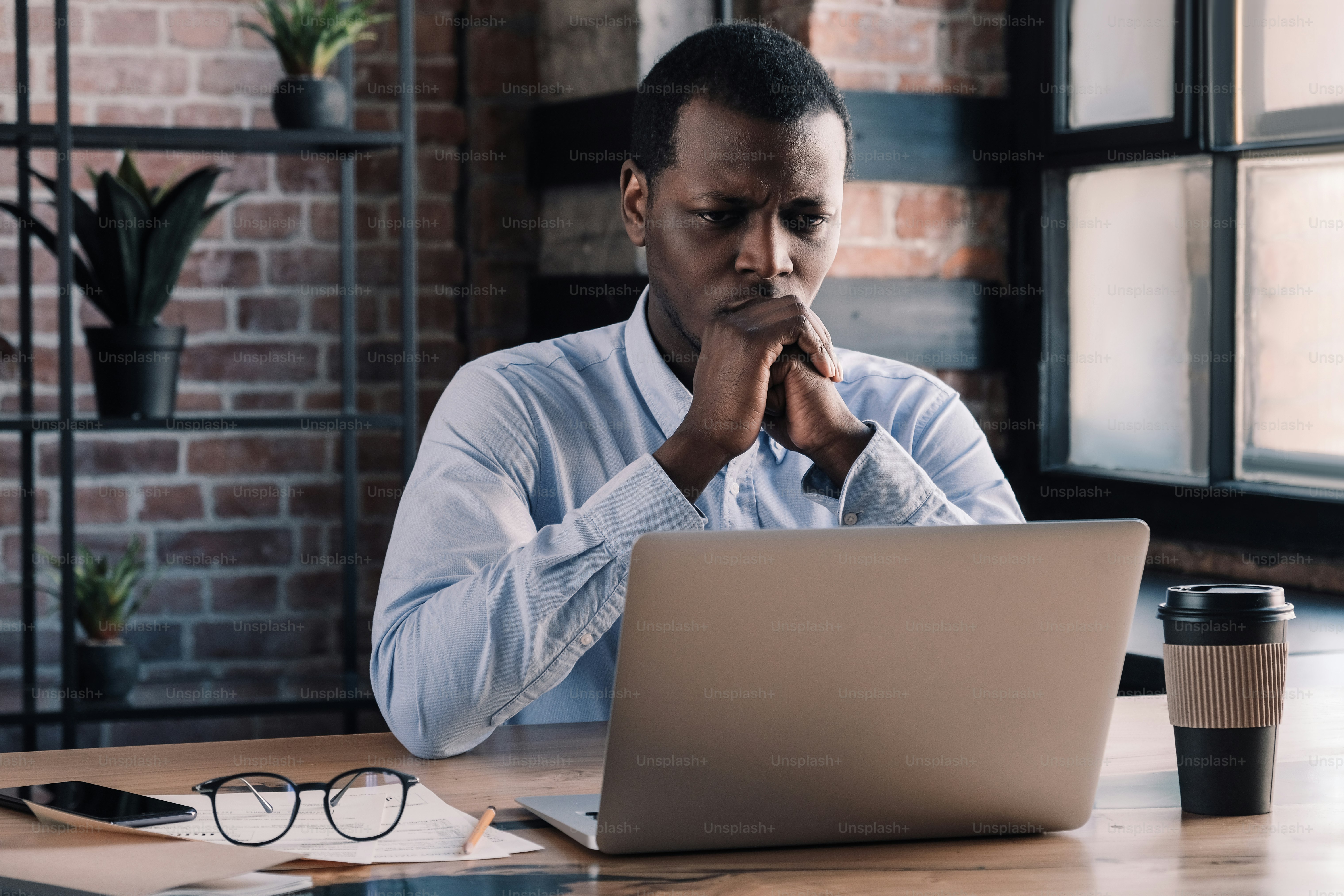Serious african american business man working on project at modern loft office, thinking about financial troubles