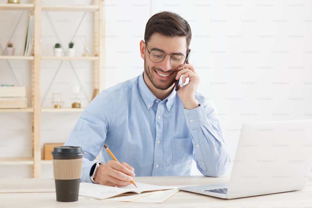 Caucasian male talking on phone and filling papers while working in office