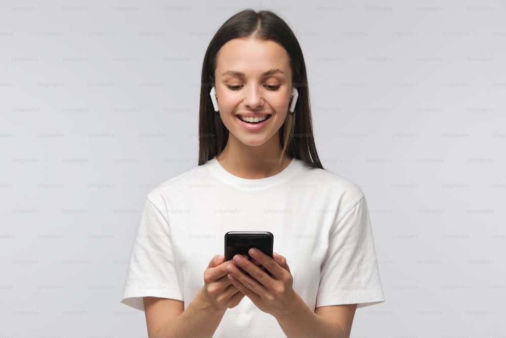 Young happy attractive european female with smartphone in hands, isolated on gray background