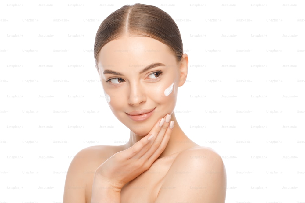 Porträt einer jungen schönen braunäugigen Frau mit Gesichtscreme auf Wangenknochen isoliert auf weißem Hintergrund, Hautpflegekonzept