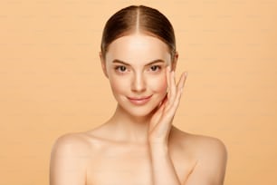 Porträt einer jungen schönen Frau mit braunen Augen und strahlender Haut, isoliert auf beigem Hintergrund. Hautpflege-Konzept