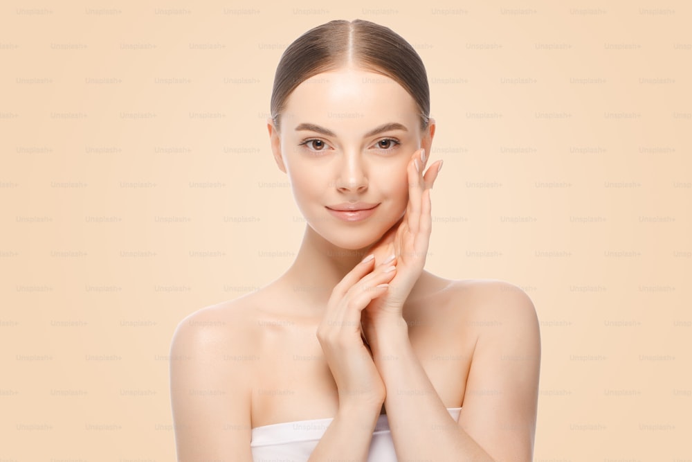 ベージュの背景に、完全にきれいな肌を持つ顔の近くに手をつないでいる女性または女性モデルの美しいポートレート。スキンケアまたは化粧品の広告。
