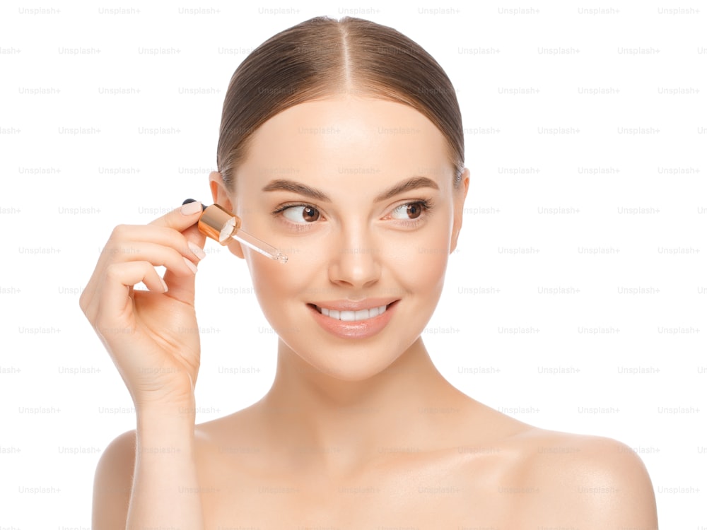 Young woman applying serum to face, looking away, isolated on white background. Beautiful model with perfect clean fresh skin. Treatment or cosmetic ads