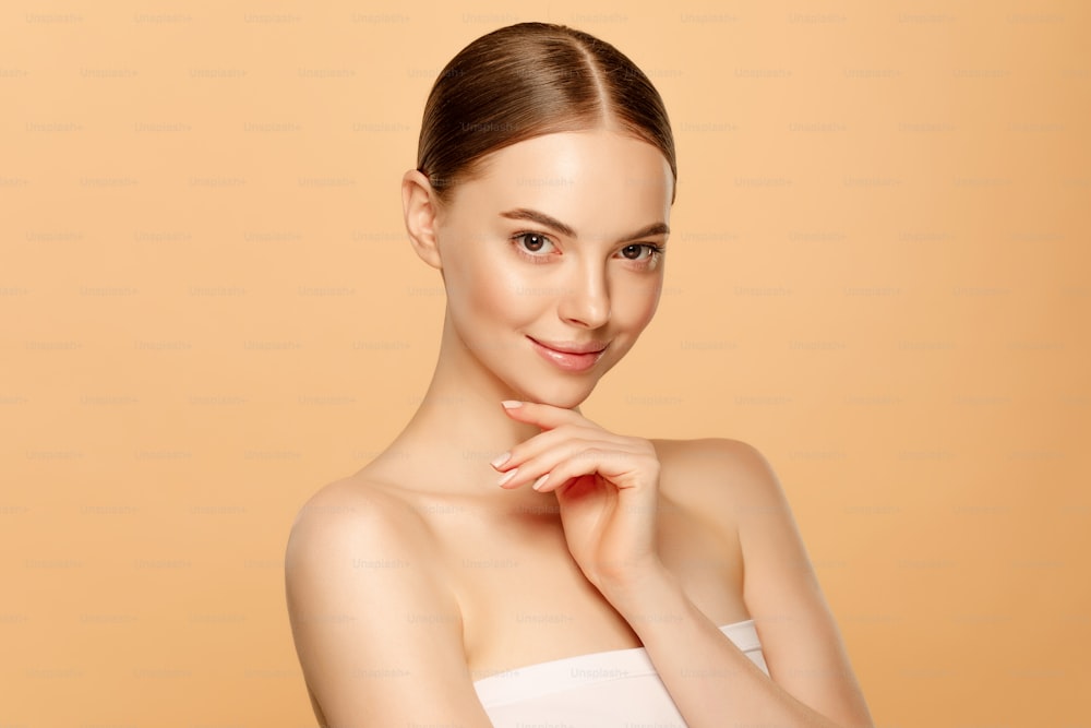 Beauty shot of young beautiful woman with brown eyes touching her chin, isolated on beige background