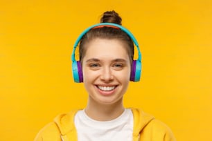 Junges lächelndes Teenager-Mädchen, das T-Shirt, Kapuzenpullover und blaue drahtlose Kopfhörer trägt, Lieblingsmusik hört und sich entspannt, isoliert auf gelbem Hintergrund