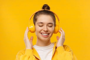 Menina nova ouvindo música através de fones de ouvido sem fio com os olhos fechados, isolado no fundo amarelo