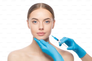 Mujer joven en clínica de belleza, lista para inyección de relleno en la mejilla para mantener la piel suave y joven, aislada sobre fondo blanco