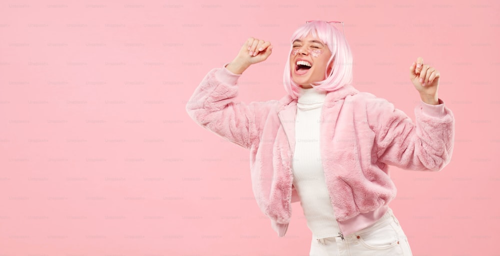 Horizontal banner of teenage girl laughing and dancing at party with closed eyes, isolated on pink background with copy space on left