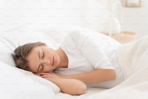 Gros plan d’une jeune femme dormant paisiblement à l’hôtel sur du linge blanc, se détendant, profitant de temps libre tard le matin, l’air calme