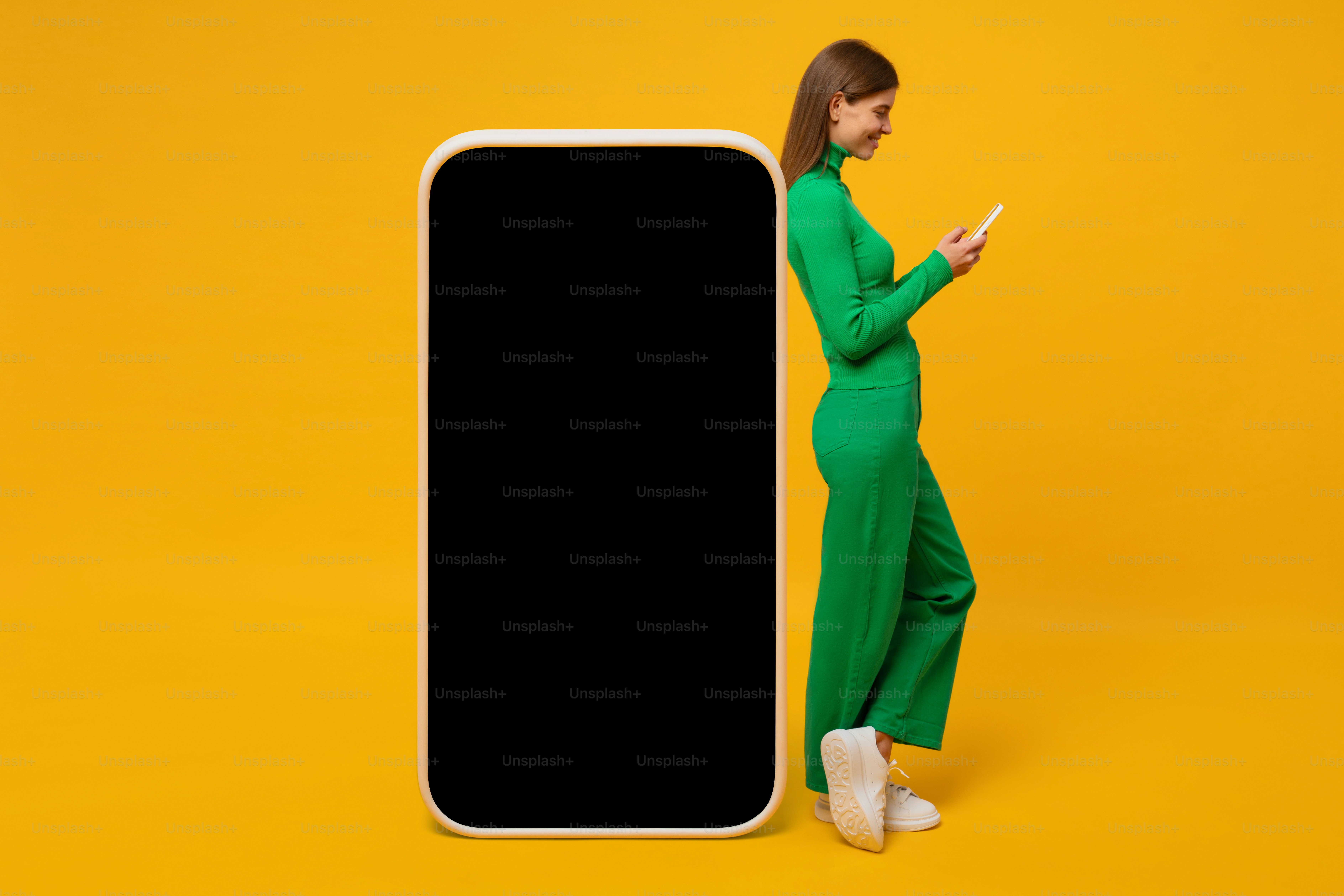 Giovane donna sorridente in piedi vicino al modello di telefono enorme per l'app, isolata su sfondo giallo